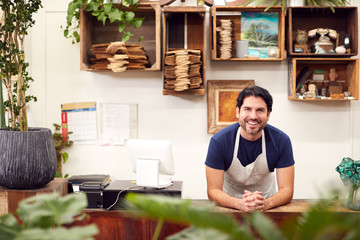 Portrait Of Smiling Male Sales Assistant Standing Behind Sales Desk Of Florists Store