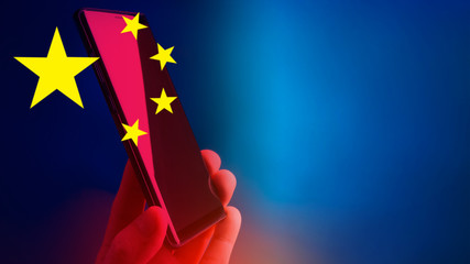 Flag of China on a blue background. A smartphone next to the Falag of the People’s Republic of...
