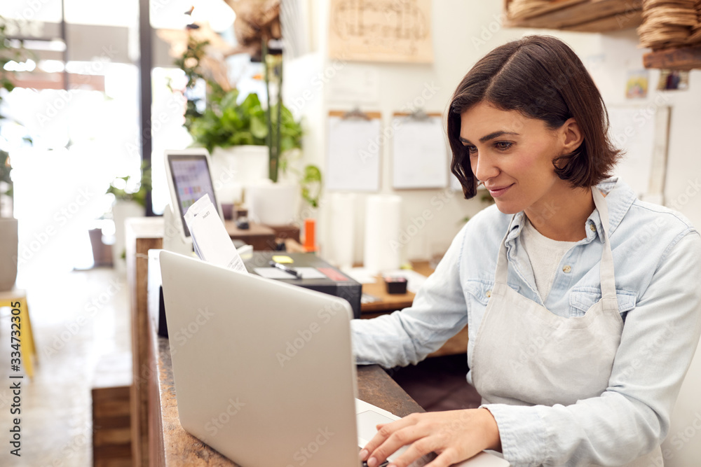 Wall mural Female Sales Assistant Working On Laptop Behind Sales Desk Of Florists Store