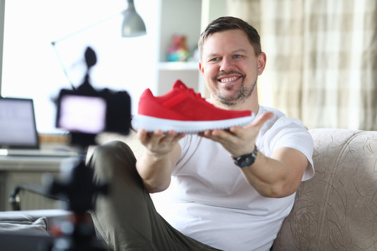 Man in an apartment is filming review new sneakers. Guy during self-isolation in apartment works remotely by shooting video blog. Guy rejoices in front camera. Interesting videos footwear