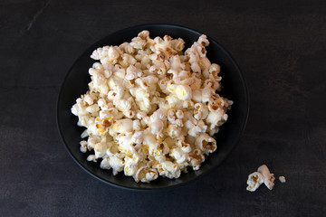 Top view of popcorn in black bowl, black background