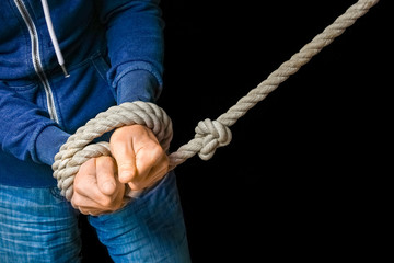 Hands tied with a rope life threatening on a black background. Slavery in business is violence against people.