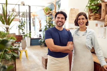 Portrait Of Smiling Male And Female Sales Assistants Standing By Sales Desk Of Florists Store