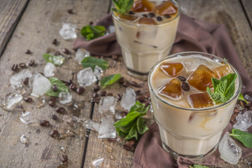Cold summer coffee, latte, frappe, frappuccino. Coffee iced cocktail drink with frozen coffee ice cubes, milk or non-dairy milk and mint leaves. Wooden background copy space