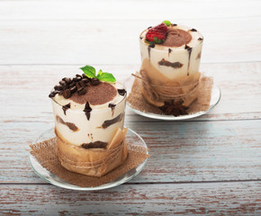 tiramisu in a glass with berries, mint and coffee beans on a light wooden background