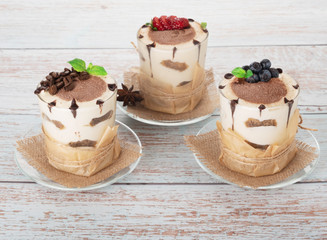 tiramisu in a glass with berries, mint and coffee beans on a light wooden background