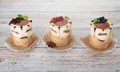 tiramisu in a glass with berries, mint and coffee beans on a light wooden background