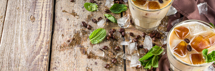 Cold summer coffee, latte, frappe, frappuccino. Coffee iced cocktail drink with frozen coffee ice cubes, milk or non-dairy milk and mint leaves. Wooden background copy space