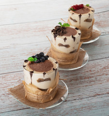tiramisu in a glass with berries, mint and coffee beans on a light wooden background