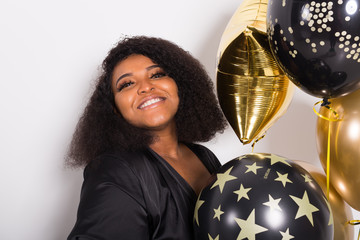 Naklejka premium Holidays, birthday party and fun concept - Portrait of smiling young African-American young woman looking stylish on white background holding balloons.