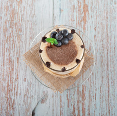 tiramisu in a glass with berries, mint and coffee beans on a light wooden background