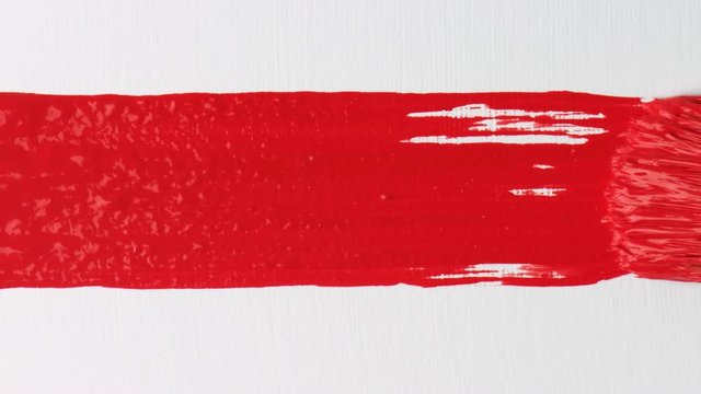 Close-up of artist holding paint brush and drawing oil painting. Painting red line on canvas.