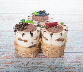 tiramisu in a glass with berries, mint and coffee beans on a light wooden background
