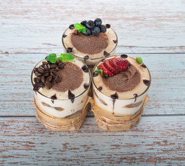 tiramisu in a glass with berries, mint and coffee beans on a light wooden background