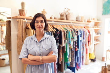 Portrait Of Smiling Female Owner Of Fashion Store Standing In Front Of Clothing On Rails