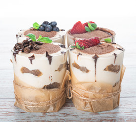 tiramisu in a glass with berries, mint and coffee beans on a light wooden background