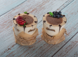 tiramisu in a glass with berries, mint and coffee beans on a light wooden background