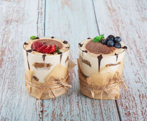 tiramisu in a glass with berries, mint and coffee beans on a light wooden background