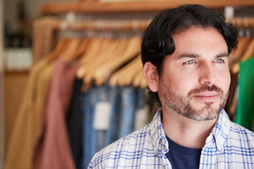 Male Owner Of Fashion Store Standing In Front Of Clothing On Rails