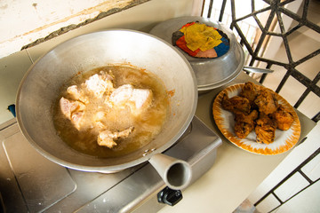 Frying a bunch of chicken in a hot boiling pan full of oil with cooked batch of chicken near it. Home style