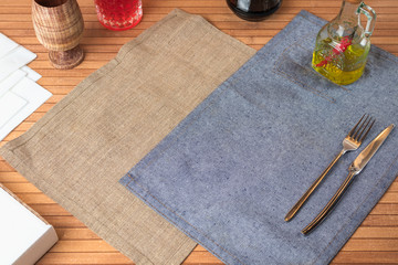 food background with a knife and fork, table covered with beige and blue napkins, sauce, drink, glass, wooden table