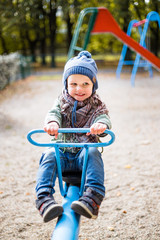 Little cheerful boy in a blue cap on a blue seesaw
