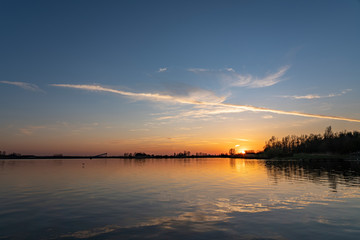 Fototapeta na wymiar A single contrail over lake Zoetermeerse Plas is illuminated during sunset in Zoetermeer, Netherlands