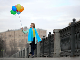 Town. Early spring. Gray city landscape. A girl with a blue scarf in bright clothes walks with balloons.