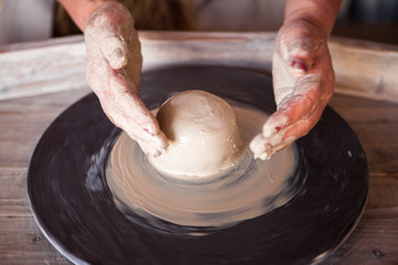 Potter's wheel with clay. Women's hands make a vase of clay.