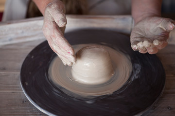 Potter's wheel with clay. Women's hands make a vase of clay.