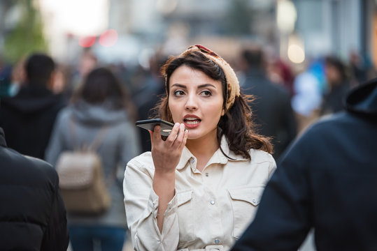 Beautiful young woman uses her smartphone voice recognition at street