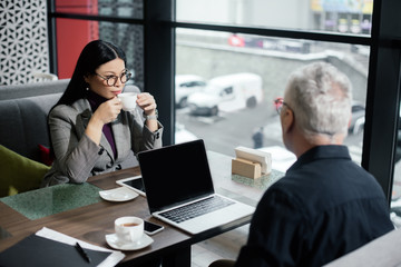 selective focus of asian businesswoman drinking tea and sitting at table with businessman