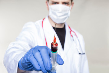 doctor holds a syringe in his hand filled with red liquid, concept of blood sampling or vaccine