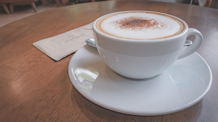 Hot coffee, white cups, plate, spoon and tissue all on the brown wooden table.