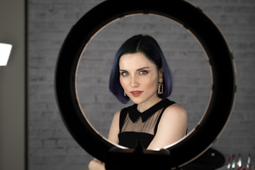 Young beautiful girl with professional makeup, blue hair and perfect skin sits in studio in front...