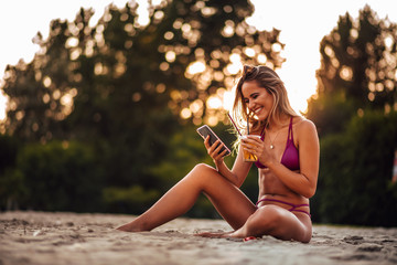 Outdoors portrait of a positive young woman using smart phone on a beach.
