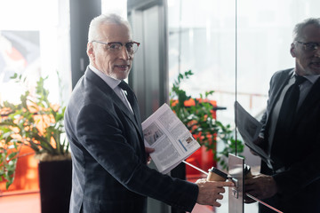 smiling businessman with newspaper and paper cup pushing button of elevator