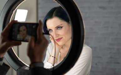 Young beautiful girl with professional makeup, blue hair and perfect skin sits in studio in front...