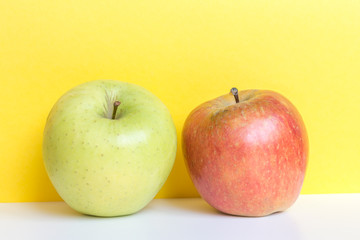 Bright red and green apples on yellow background and white table.