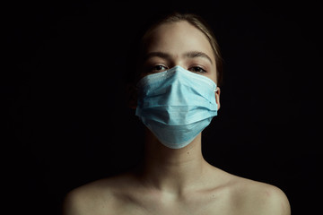 Dramatic light illustration of coronavirus epidemic. Girl with protective mask. Black background. Concept of quarantine.