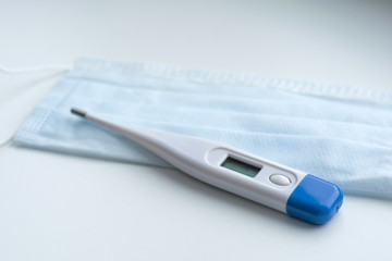 Thermometer on a medical mask in blue on a white background. Coronavirus Precautions Mask Protection.