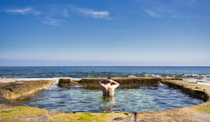 Young man enjoying a natural swimmingpool from sea water, enjoying open water space and warm calm water. with sea view