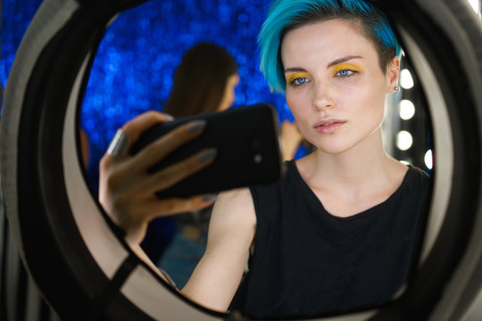 Girl With Blue Hair And Yellow Eye Makeup Take A Selfie On The Phone In A Beauty Studio In Front Of A Ring Light On Social Media.