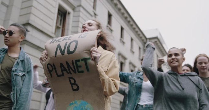 Group of demonstrators marching on the streets with a signboard to save earth and giving slogans. People with placards and posters on a global strike for climate change.
