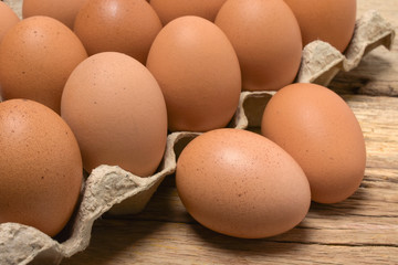 Raw chicken eggs in carton box on wooden table.