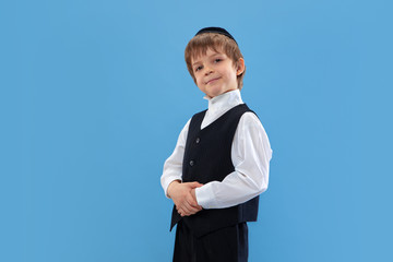 Posing confident, cute. Portrait of a young orthodox jewish boy isolated on blue studio background....