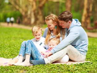 Naklejka na ściany i meble Happy family in sunny summer park having fun together on grass, leisure lifestyle of parents with children