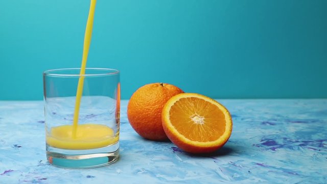 orange juice is poured into a drinking glass on blue background. Side view, close up, copy space, slow motion.