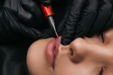 Professional master cosmetologist makes a tattoo of beautiful lips. Macro close-up shot