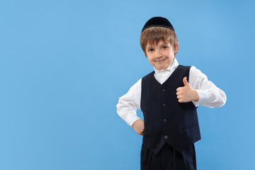 Thumb up. Portrait of a young orthodox jewish boy isolated on blue studio background. Purim, business, festival, holiday, childhood, celebration Pesach or Passover, judaism, religion concept.